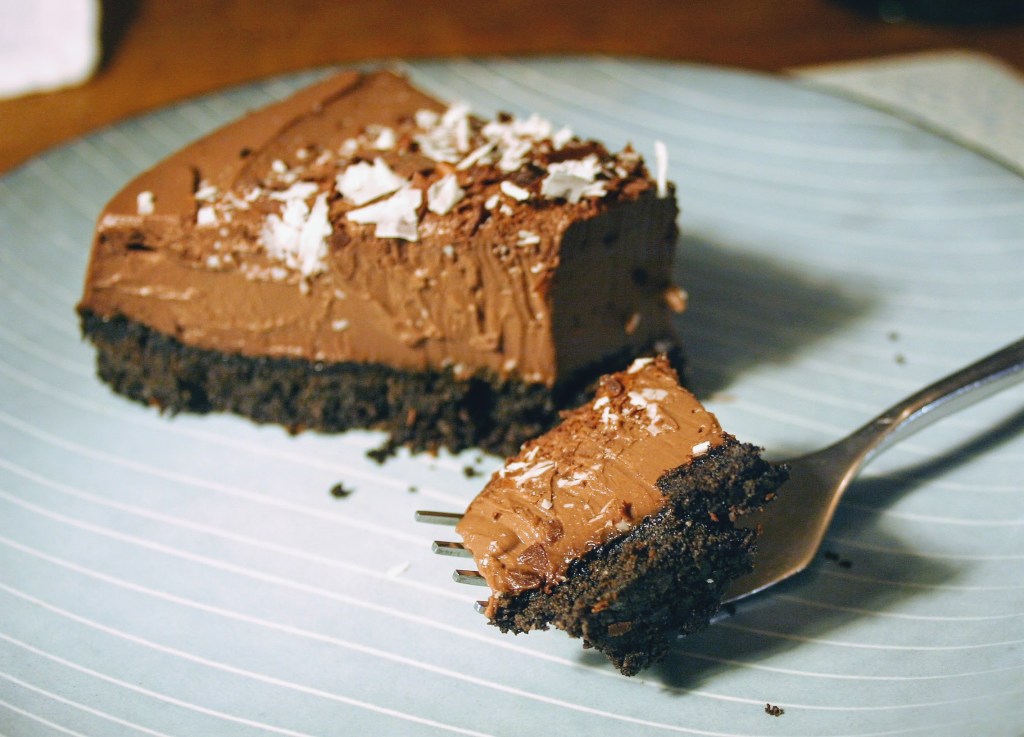 A forkful of vegan chocolate tart with a dark chocolatey biscuit base and smooth, creamy chocolate filling 