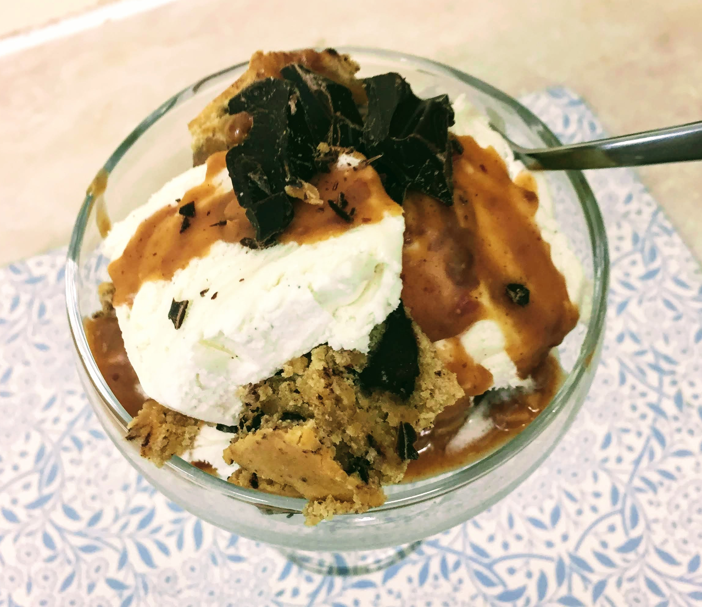 A cocktail glass filled to the brim with cubes of vegan and gluten-free chocolate chip blondies, vegan vanilla ice-cream, doused in caramel sauce, and scattered with dark chocolate chunks.