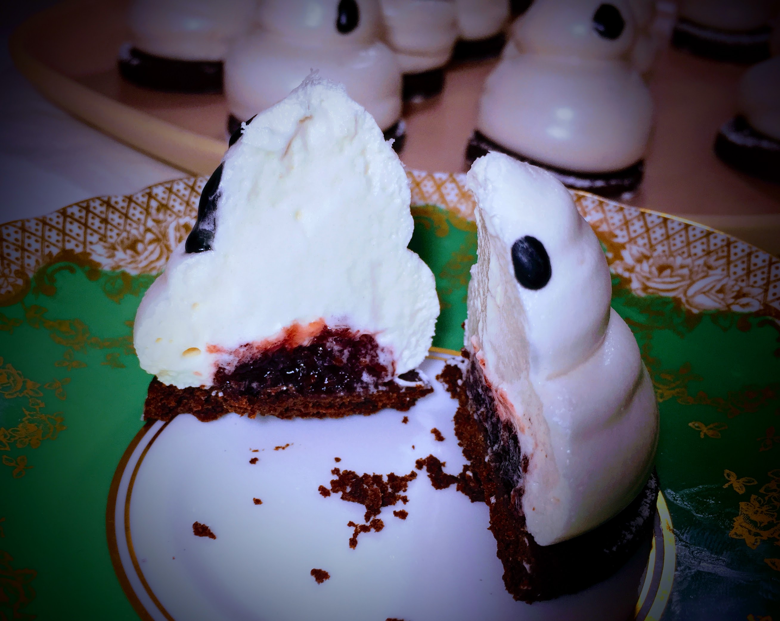 A vegan marshmallow ghost biscuit cut in two. The marshmallow is sliced smoothly to reveal a red jam centre.