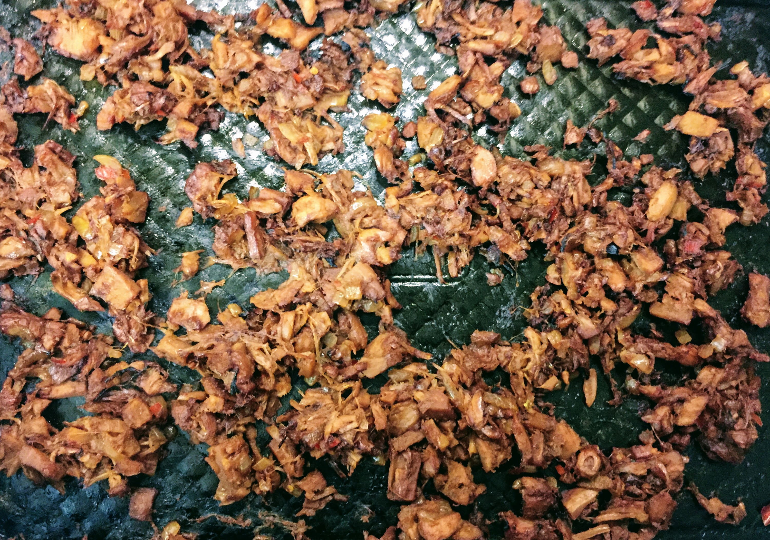 An aerial view of the tamarind pulled jackfruit once it has been taken out of the oven. All the liquid has dried up but the jackfruit chunks are still juicy and flakey and a lovely reddish brown colour. The chunks are charred in places from the heat of the oven. 