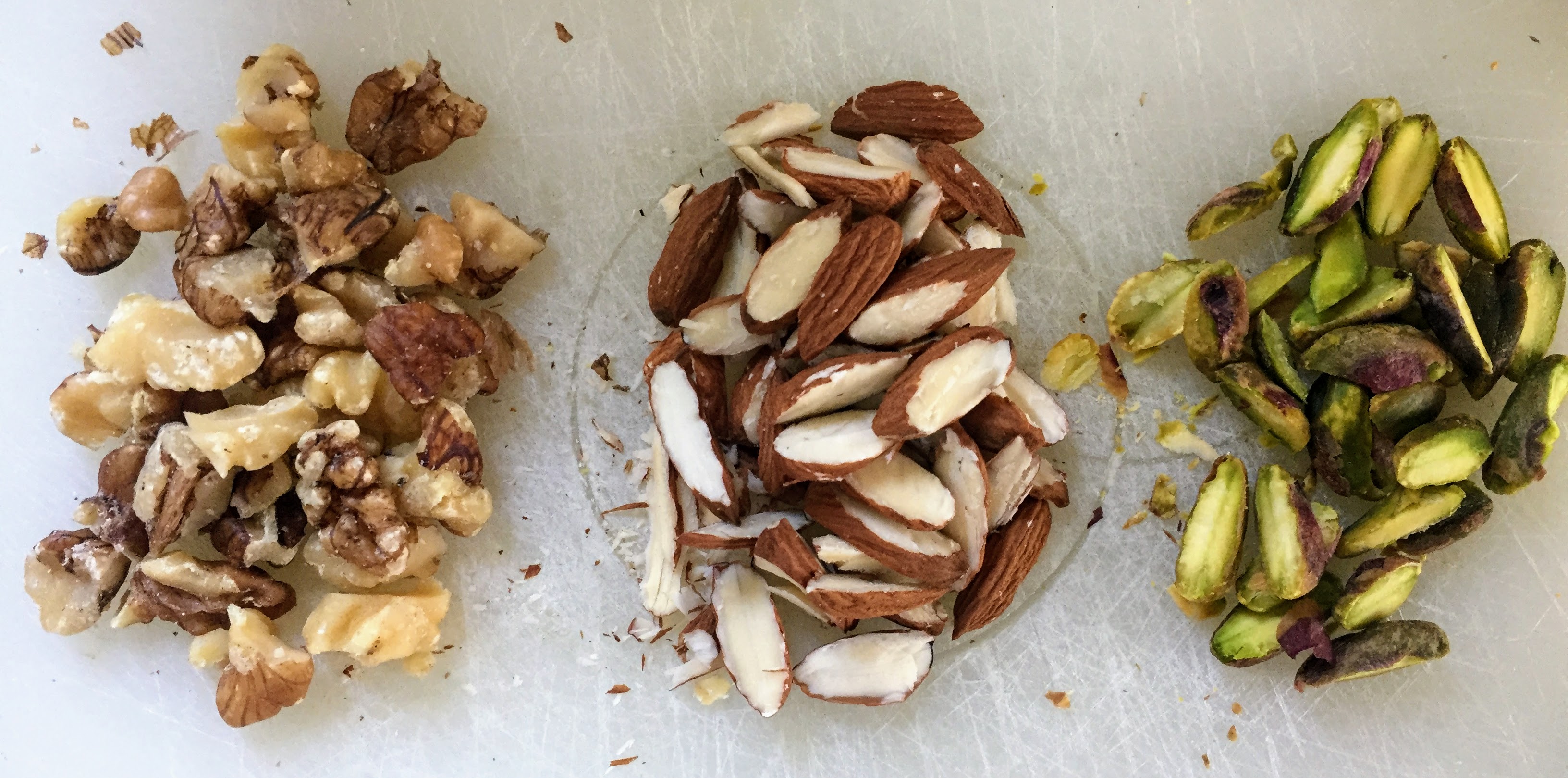 Three small piles of chopped walnuts, slivered almonds, and halved pistachios.