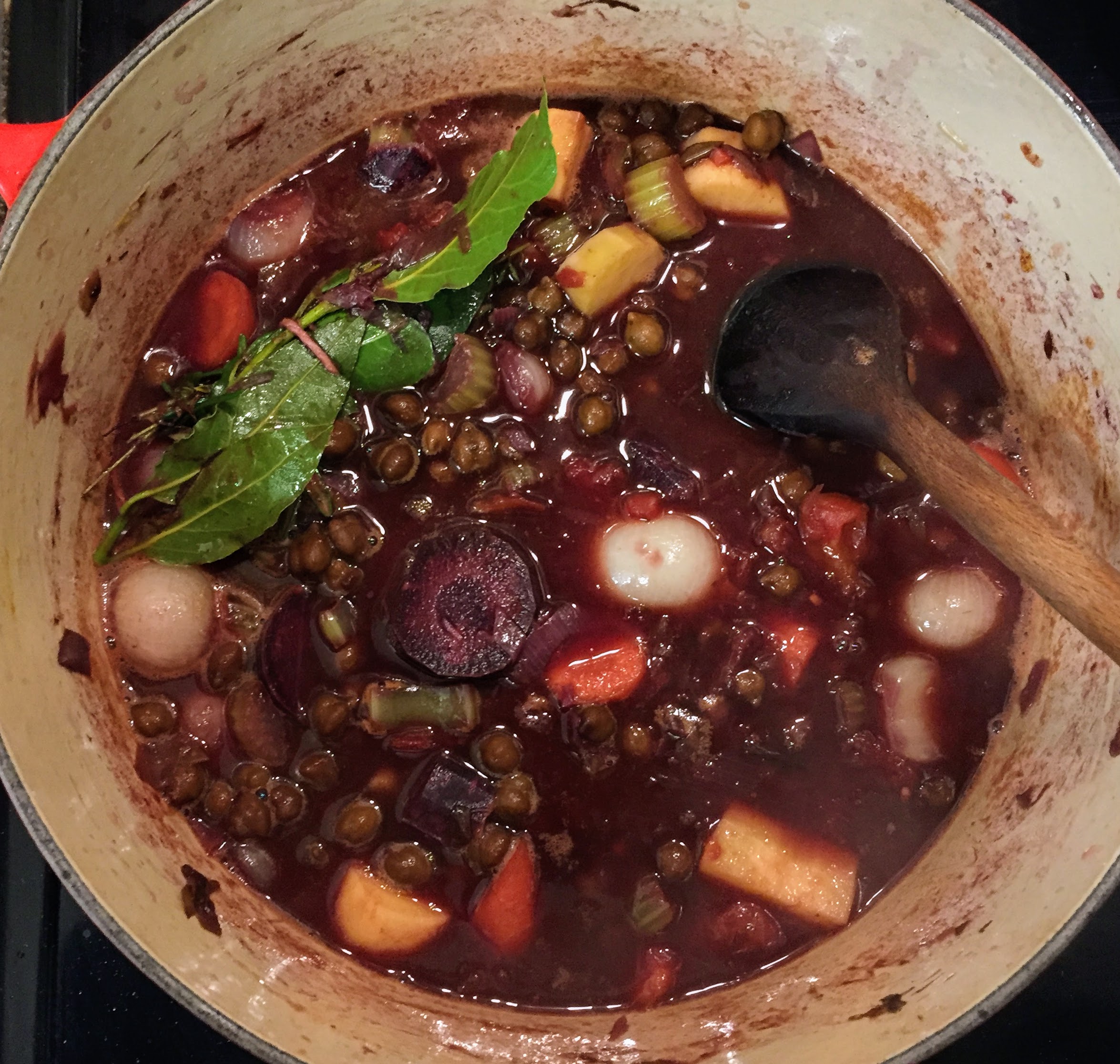 A birdseye view of the casserole dish before it goes in the oven. The stock is quite thin and the vegetables are firm and distinct, before being stained purple after slow-cooking in the oven. A bundle of bay leaves, rosemary, and thyme floats on top, tied with some string.