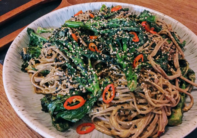 A close up of the noodles - soba noodles have a darker colour than regular noodles due to the added buckwheat. The noodles are shiny with sesame sauce, and the cooked purple sprouting leaves have turned an even darker green, next to the vibrant broccoli stalks.  