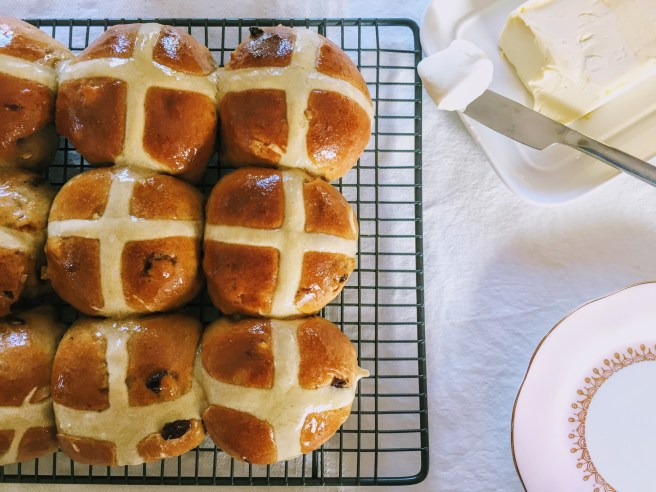 Shiny, golden brown hot cross buns on a wire cooling rack, ready to be savoured.