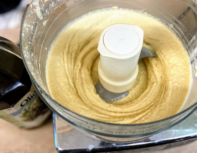 Thick and creamy hummus in a food processor, still with a little texture, after the olive oil has been added.