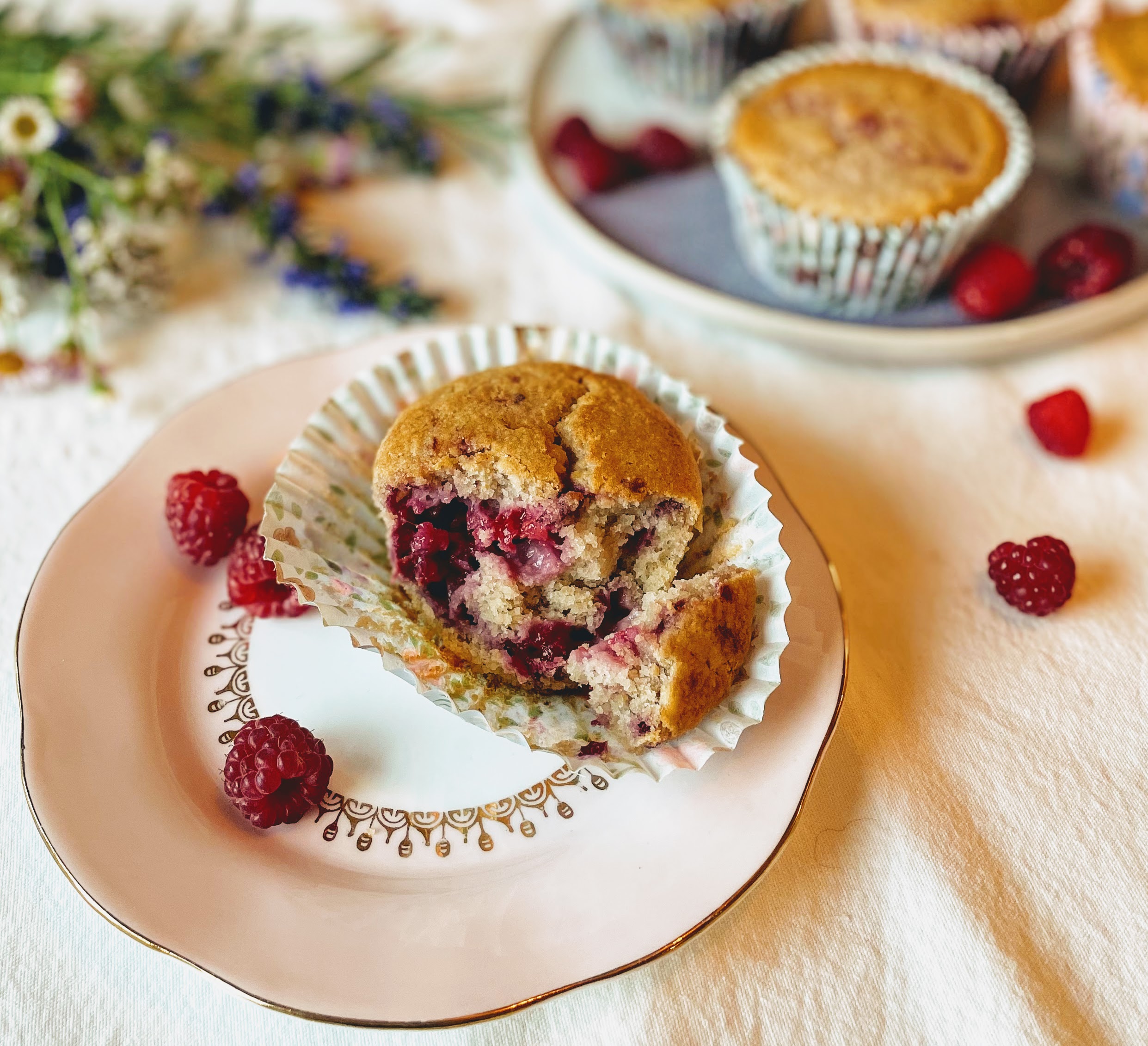 A lemon and raspberry muffin split in half. The sponge is light and delicate, and interspersed with pockets of vibrant and glistening cooked raspberry. 