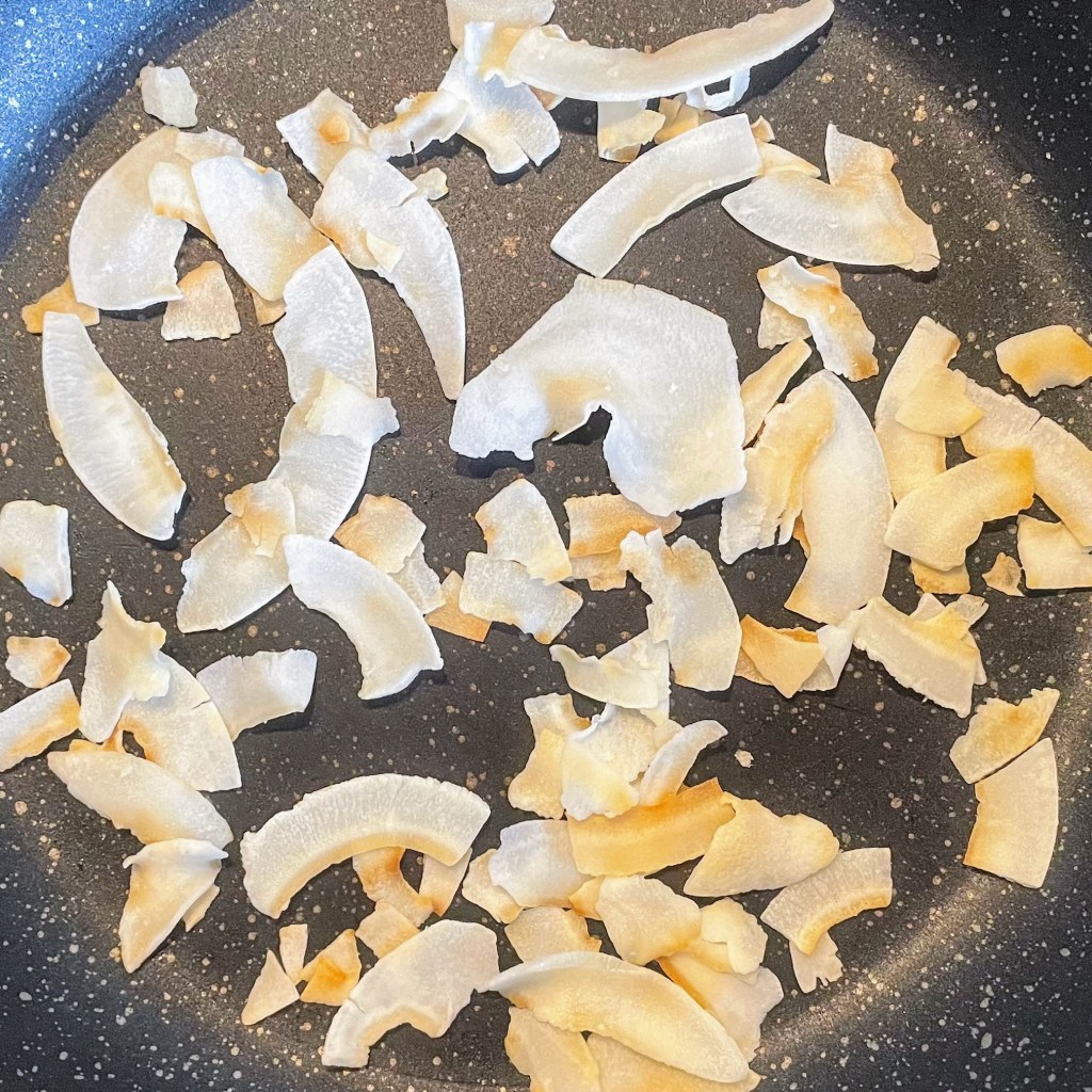 Coconut flakes in a dry frying pan, just starting to turn golden.